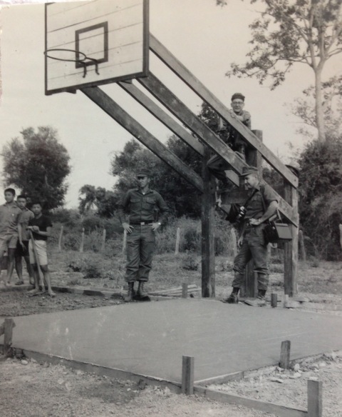 A vintage photo of army men standing beside a basket ball pole